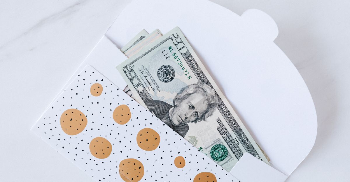 Top view of open carton money envelope with pile of paper money for birthday gift on white table