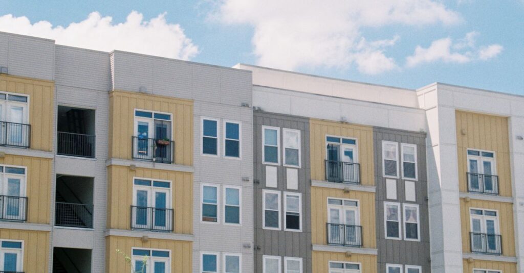 Contemporary apartment building exterior with yellow and grey panels under a clear blue sky.