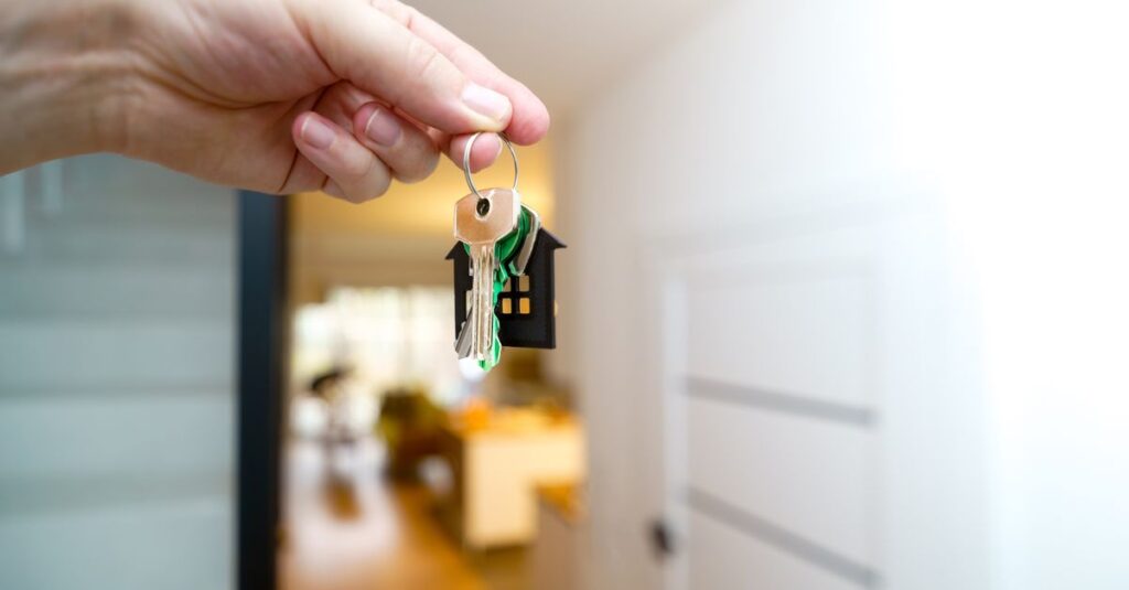 A hand holding house keys inside a modern apartment, symbolizing new property ownership or rental.