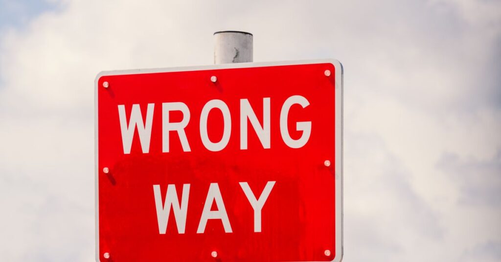 Clear image of a bright red 'Wrong Way' traffic sign against a cloudy sky in Miami, Florida.