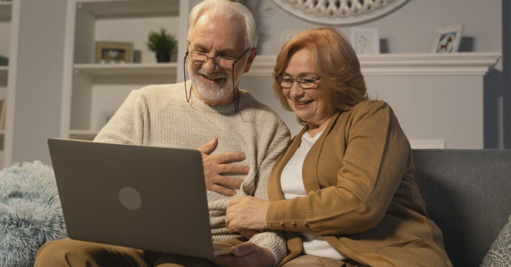 Happy senior couple sitting on a sofa having a joyful video call on a laptop in a cozy living room.