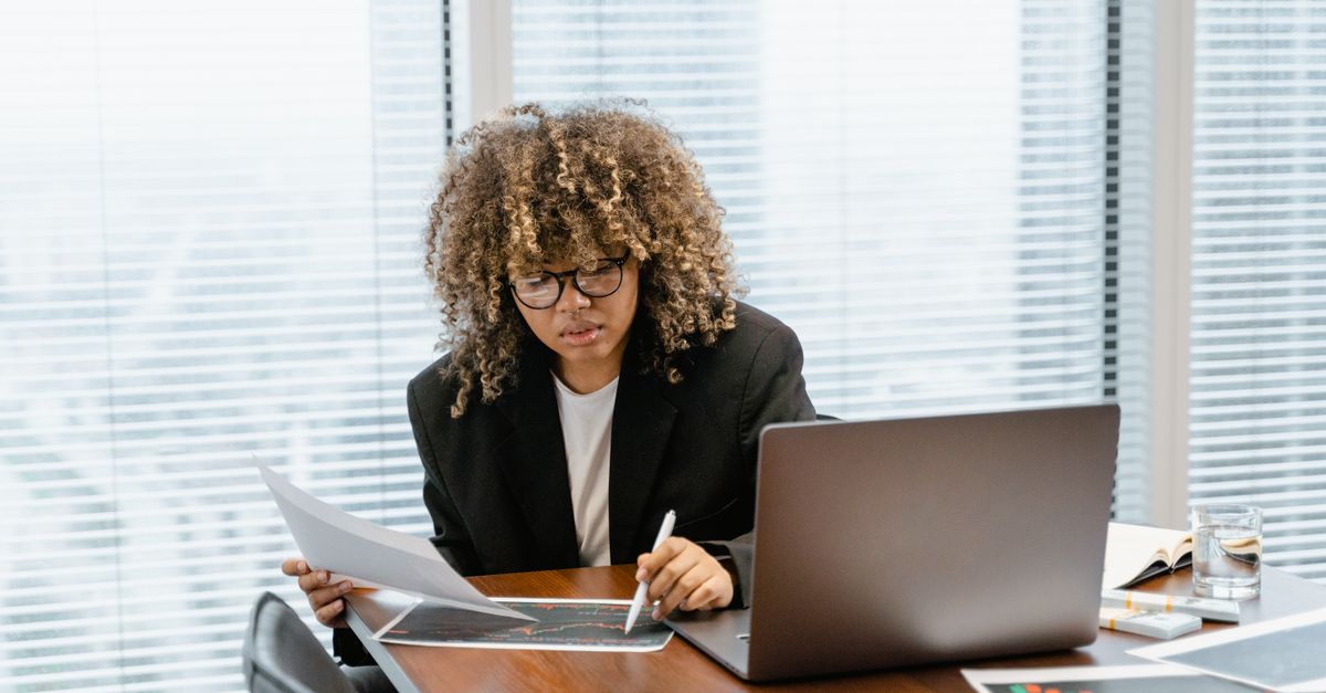A young professional analyzing financial charts at a modern office desk with a laptop.