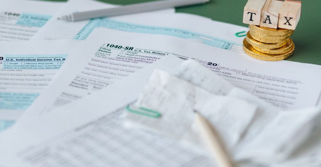 Stack of tax forms and coins with a 'TAX' stamp, symbolizing finance and accounting.