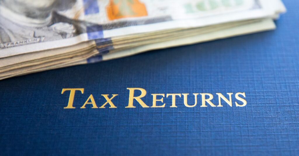 Close-up of tax returns folder beside a stack of American dollars, representing finance and accounting.