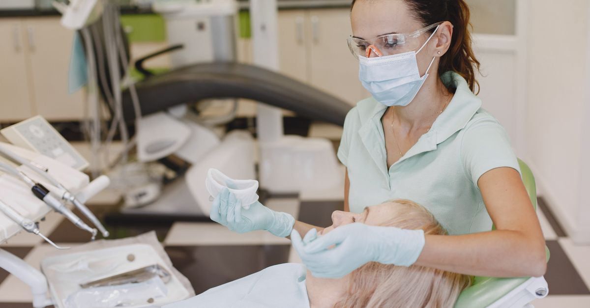 Female dentist with face mask examines patient in modern clinic. Healthcare setting.