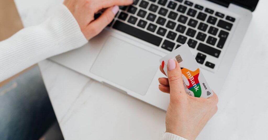Close-up of a person using a laptop and holding a credit card for online shopping.