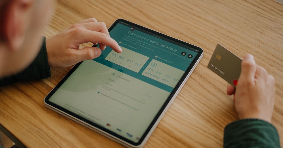 Person making an online payment using a tablet and credit card on a wooden desk.