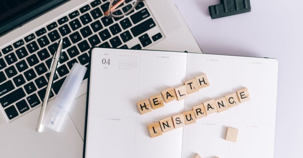Scrabble tiles spelling health insurance on a planner next to a laptop.