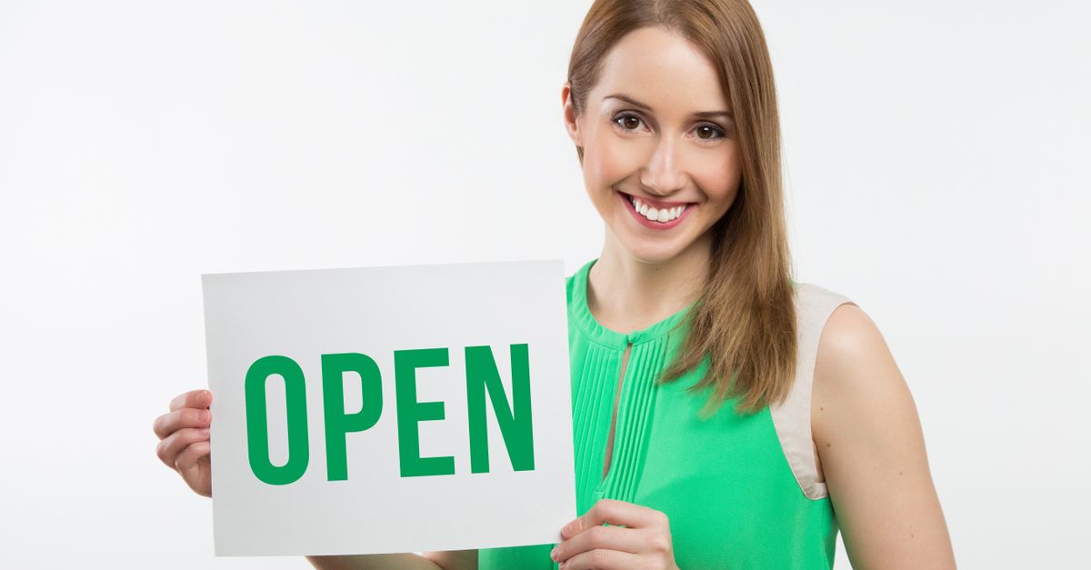 Cheerful woman in green holding an open sign, perfect for business use.