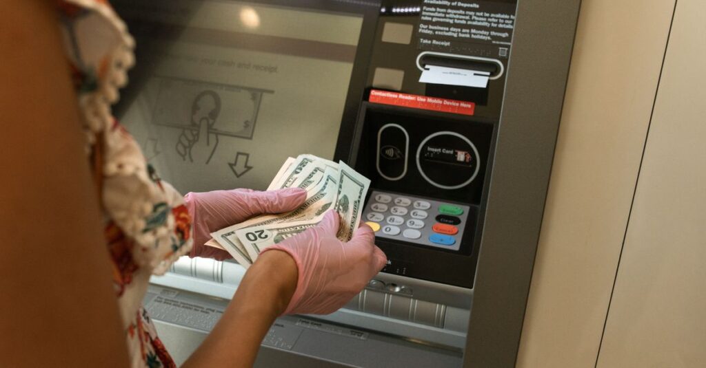 A person wearing gloves withdraws cash from an ATM, ensuring hygiene.