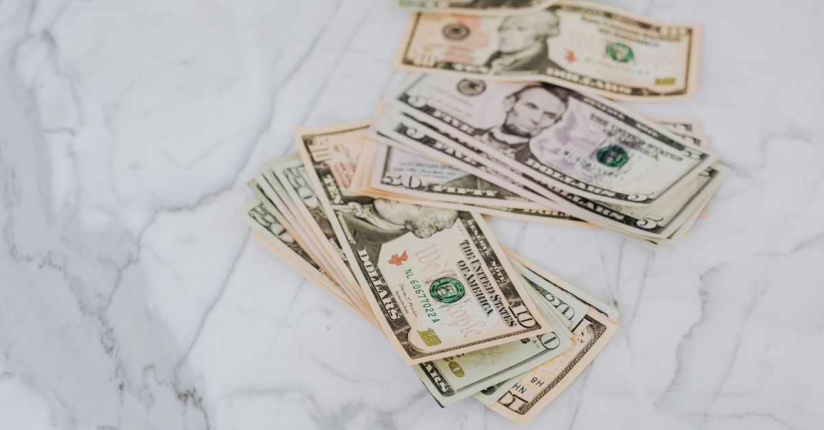 A stack of US dollar bills spread on a marble surface, representing wealth and finance.