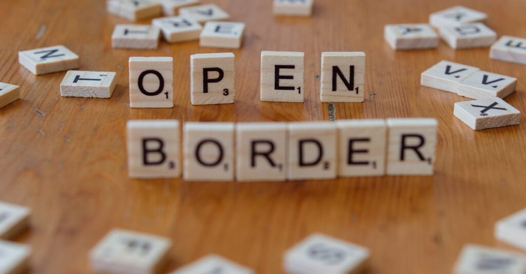 Wooden Scrabble letters on a table spelling out 'open border', concept of migration and geopolitics.