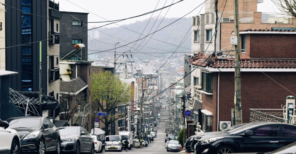 Street view of Seoul with parked cars and urban architecture on a cloudy day.
