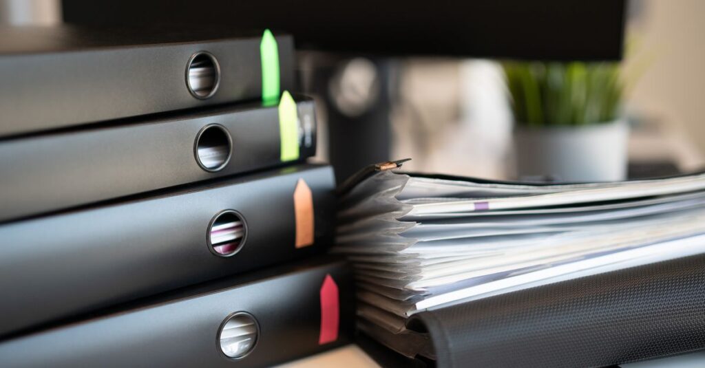 Stack of colorful ring binders and documents on a modern office desk setting.