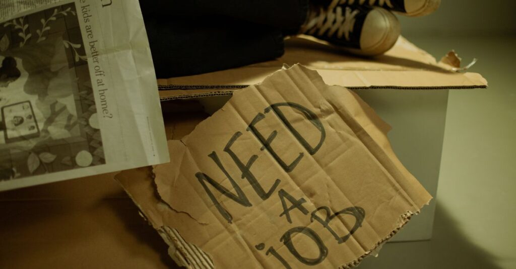 Close-up of a cardboard sign and newspaper depicting joblessness and unemployment.