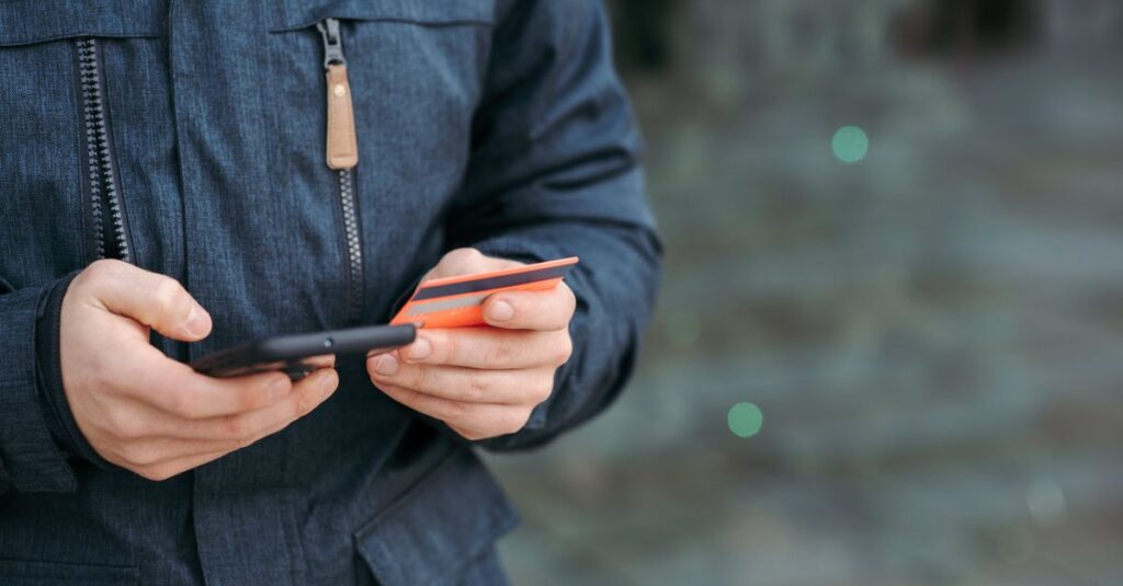 Crop anonymous male in casual clothes entering credit card details on smartphone on street in daylight
