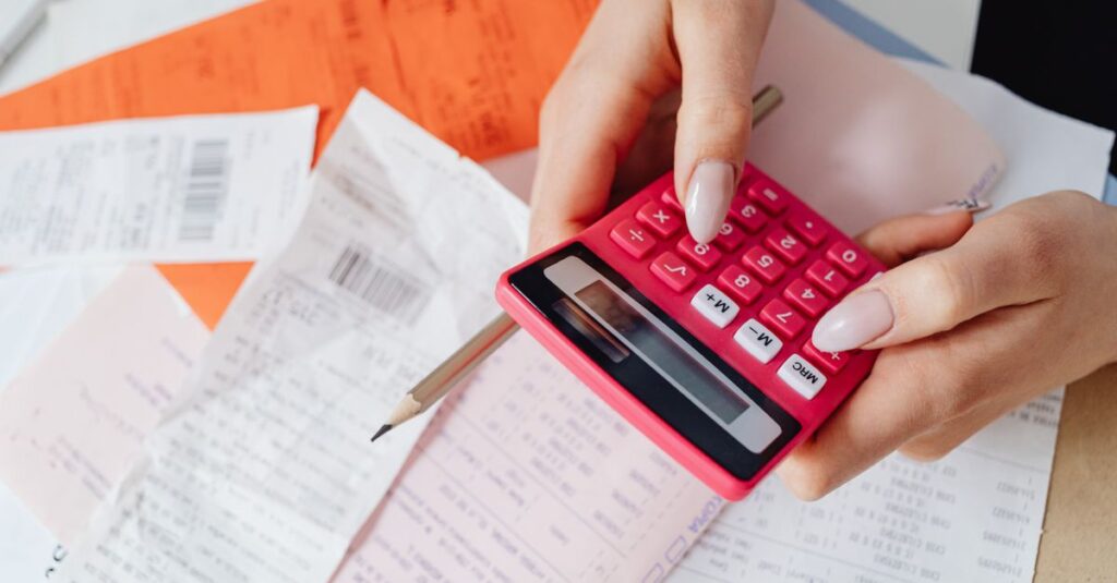 Hands using a pink calculator to manage expenses amidst various receipts and documents.