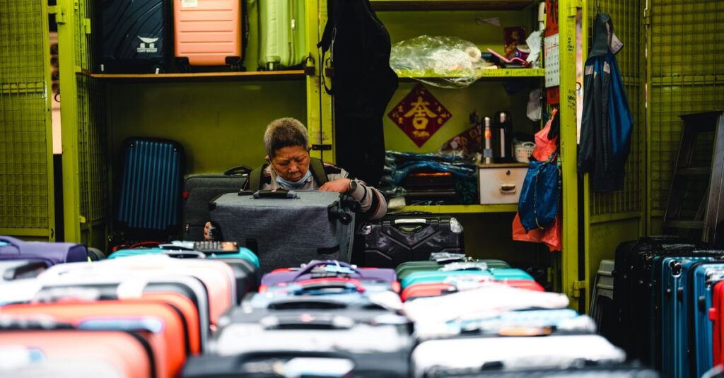 A vendor arranges colorful suitcases in a vibrant market store setting.