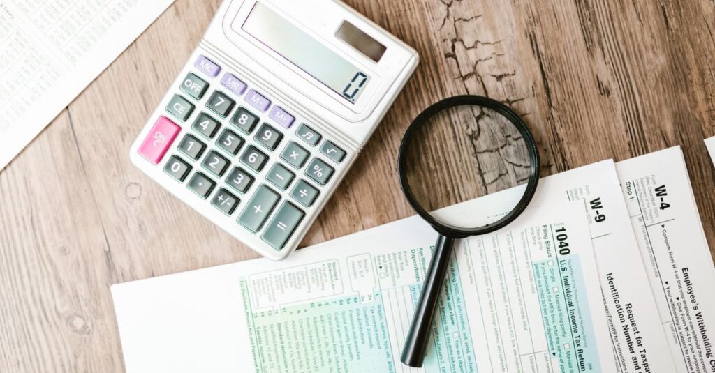 Tax forms laid out with a calculator and magnifying glass on a wooden surface, perfect for finance themes.