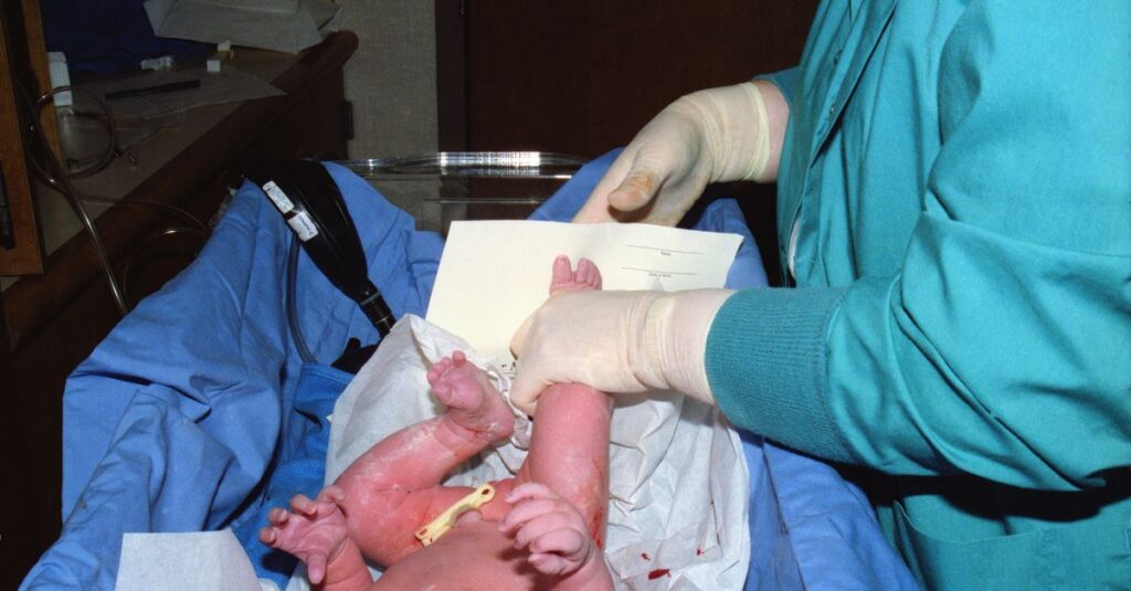A nurse tends to a newborn baby in a hospital delivery room setting.
