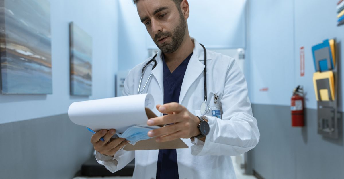 Male doctor in hospital hallway reviewing medical charts, focused and dedicated.