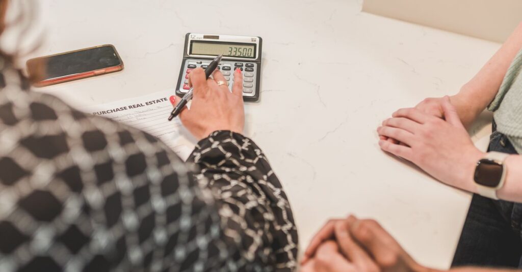 Close-up of hands during a real estate transaction with a calculator and purchase document on the table.