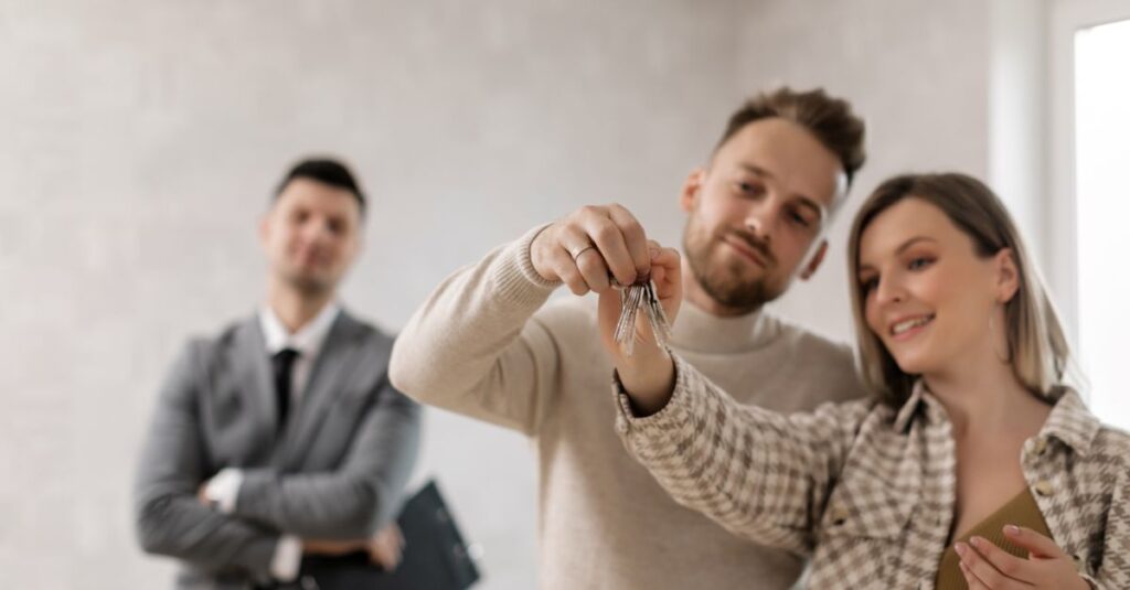 A joyful couple holding keys to their new home with a realtor in the background.