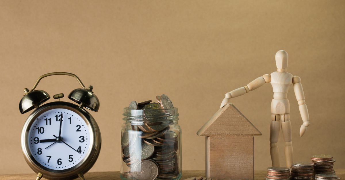 Wooden mannequin with a house, coins, and clock symbolizing time and financial planning.